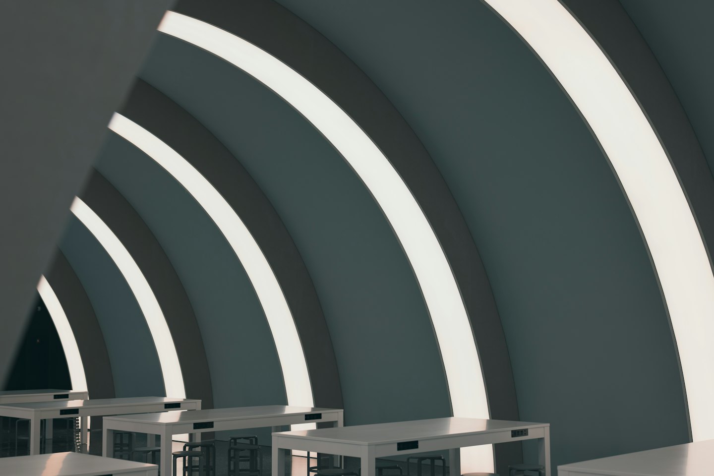 Gekromde muren met stripverlichting en witte tafels in een moderne coworking space.